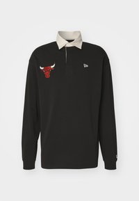 Polo noir à manches longues avec un col beige, comportant un logo de taureau rouge brodé sur la poitrine et un petit logo blanc sur la manche.