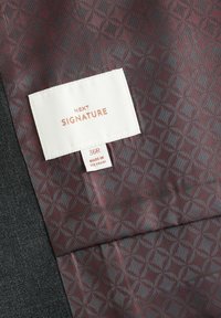 Clothing label reading "NEXT SIGNATURE" and "36R MADE IN VIETNAM" on patterned maroon and gray fabric next to dark gray textile.