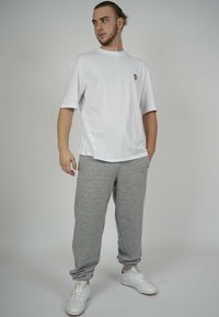 White cotton t-shirt with a small black logo, paired with gray sweatpants made of fleece. Model wears white sneakers with tan soles.