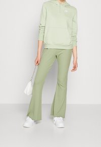 Ljusgrön hoodie med känguruficka och logotyp. Matchande ribbade utsvängda byxor och vita sneakers. Vit handväska med kedjestropp.