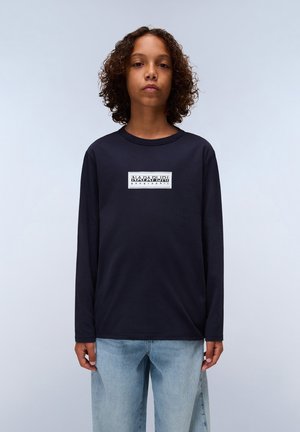 Marineblaues Langarm-T-Shirt mit einem rechteckigen grafischen Logo in Weiß auf der Brust, kombiniert mit hellblauen Denim-Jeans im entspannten Schnitt.