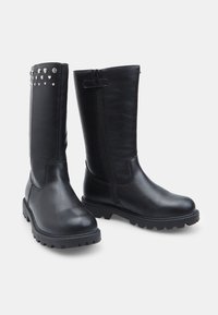 Stivali neri in pelle al ginocchio con texture liscia, suole rigate, cerniera laterale e borchie decorative a forma di cuore sulla parte superiore.