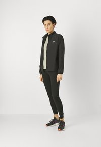 Sort letvægtsjakke med høj krave, parret med en lys bluse og sorte leggings. Sorte sneakers med lilla accenter fuldender looket.