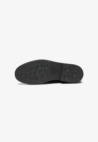 Suela de zapato de goma negra con una superficie lisa, que presenta patrones de agarre circulares y puntos elevados, marcada con "ZIGN" y tamaño "45".
