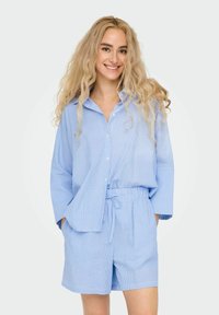 Blauw gestreepte knopshirt met losse mouwen, gecombineerd met korte broek met elastische taille, beide gemaakt van lichtgewicht stof.