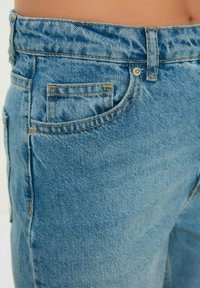 Jeans de mezclilla azul claro con una cintura alta, diseño clásico de cinco bolsillos y costuras visibles. Textura suave con un acabado ligeramente desgastado.