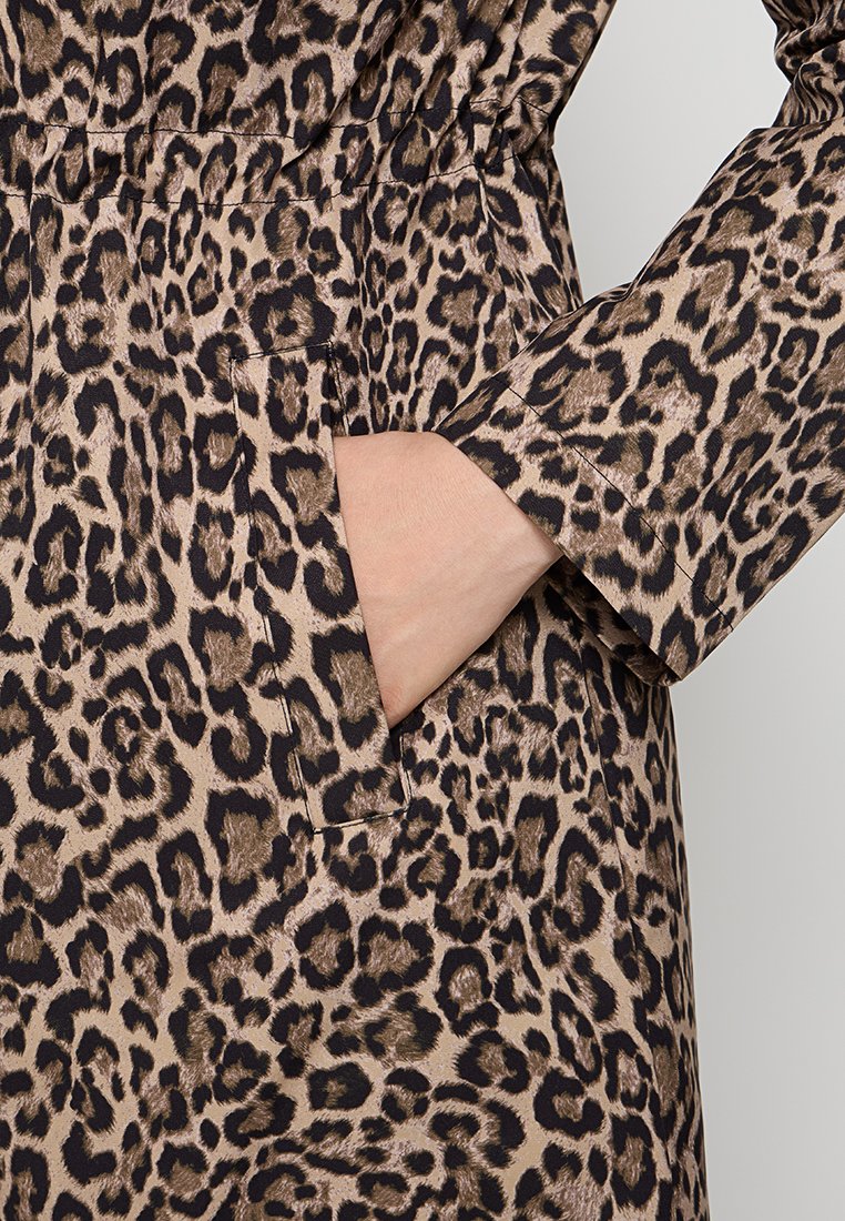 Tissu à imprimé léopard avec un motif beige et noir. Présente une poche latérale et des manches longues, avec une surface lisse et texturée.