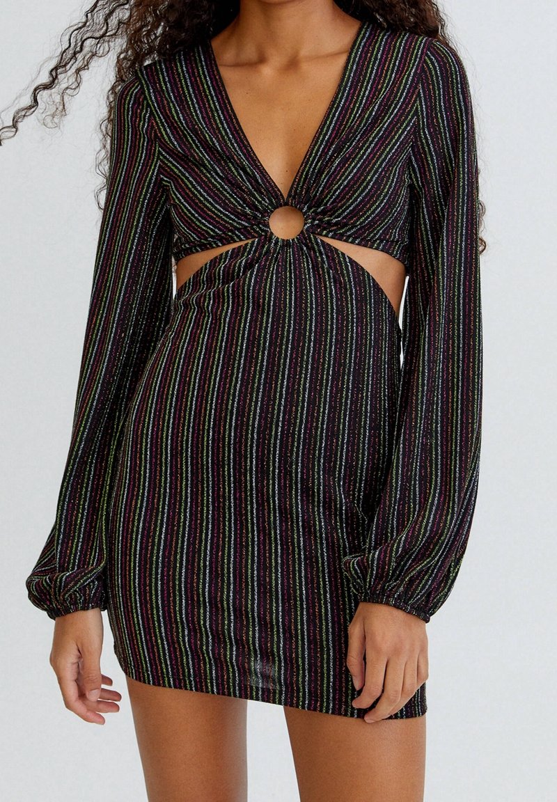 Femme portant une mini-robe noire à manches longues avec des rayures verticales multicolores, une découpe en forme de trou de serrure à l'avant et des manches froncées.