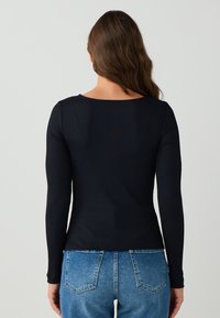 Schwarzes langärmliges Rippoberteil mit Rundhalsausschnitt, figurschmeichelndem Design und weichem Material, kombiniert mit hochgeschnittenen blauen Jeans mit Gesäßtaschen.