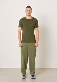 Olivno zelena majica s kratkimi rokavi, kombinirana z ohlapnimi svetlo zelenimi hlačami. Obleka ima sproščen kroj in preprost dizajn. Vključene so športne superge.