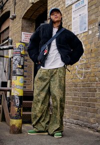 Črno prešito jakno, belo majico, ohlapne zelene hlače s kamuflažnim vzorcem in zelene čevlje. Dodatki vključujejo modro kapo in torbo čez ramo.