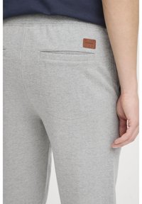 Lys grå joggingbukser med en blød tekstur, der har baglomme og et brunt lædermærke med "BLEND" branding. Elastisk talje inkluderet.