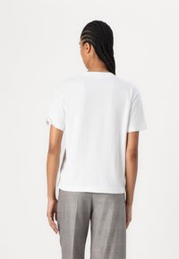 Weißes Baumwoll-T-Shirt mit kurzen Ärmeln und umgeschlagenen Bündchen, ausgestattet mit einem klassischen Rundhals und einem lockeren Schnitt. Getragen mit grauen karierten Hosen.