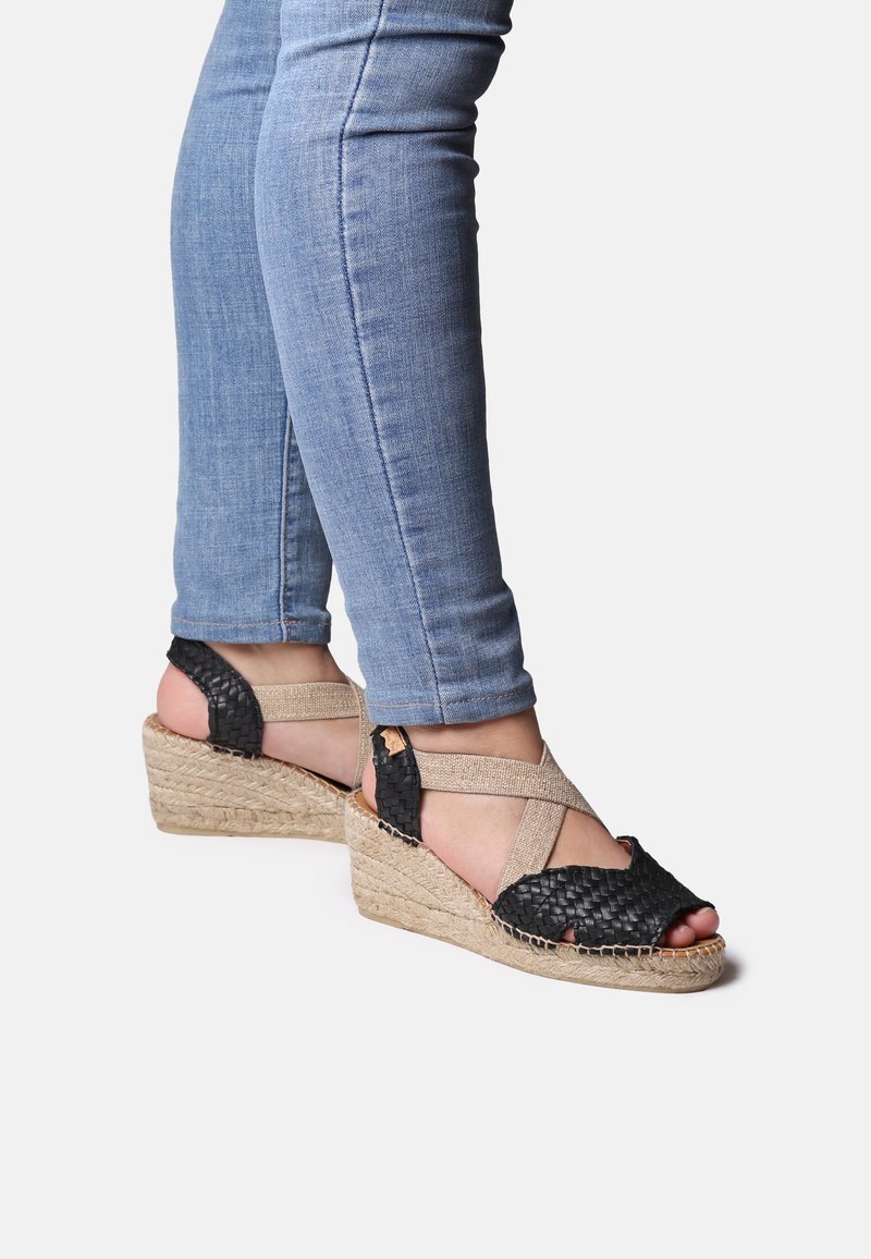 Sandali a wedge neri intrecciati con cinturino incrociato beige, caratterizzati da una base in rafia intrecciata naturale e design con punta aperta.