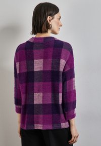 Purpurowo-różowy sweter w kratkę z rękawami o długości trzech ćwierć, z teksturowanej tkaniny i luźnym krojem. Miękki, puszysty materiał z okrągłym dekoltem.