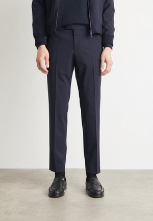 Pantaloni navy dalla vestibilità slim, con una texture liscia e pieghe sottili. Abbinati a scarpe di pelle nera e una giacca coordinata.