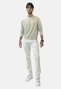 Sweat-shirt beige clair avec un col rond, associé à un pantalon slim blanc et des baskets blanches. Texture lisse et éléments de design minimalistes.