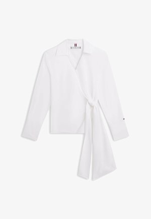 White long-sleeve wrap blouse with collar and side knot detail, featuring a small logo on the cuff and inside neck label.