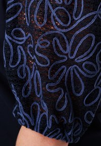 Marineblauwe stof met ingewikkelde bloemenborduurwerk in lichtblauw, met een textuur van kant en een elastische manchette voor een goede pasvorm.