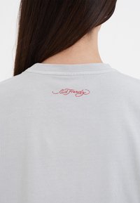 Lichtgrijze katoenen T-shirt met ronde hals en geborduurd "Ed Hardy" logo in het rood op de achterkant, met een soepele textuur.