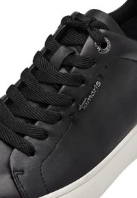 Sneaker nera in pelle con superficie testurizzata, lacci tonali e accento del logo argentato. Presenta una suola in gomma bianca.