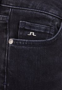 Mörkblå denimjeans med en framficka, silverdetaljer och en liten silverlogotyp på fickan. Texturerad tyg.