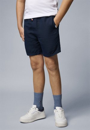 Pantalones cortos azul marino con cintura elástica y bolsillos laterales, combinados con zapatillas blancas y calcetines azules con un pequeño logotipo.