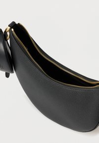 Svart läderväska med en strukturerad yta, böjd form och gulddetaljer på dragkedjan. Inkluderar en liten fastsatt ficka.