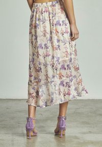 Jupe midi florale en tissu léger et transparent crème, ornée de fleurs violettes et orange ; assortie à des sandales à talons en daim lavande.