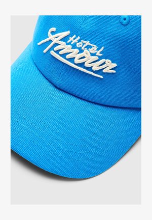Gorra de béisbol azul brillante con texto bordado en blanco "Hotel Amour" en el panel frontal, mostrando tela texturizada y visera curvada.