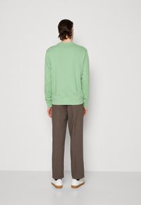 Muntgroene sweatshirt met geribbelde manchetten en zoom, in combinatie met bruine broeken en witte sneakers, gezien vanuit de achterkant.