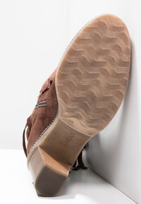 Stivaletto alla caviglia in camoscio marrone con suola in gomma, caratterizzato da un motivo a zigzag antiscivolo e un tacco di media altezza. Chiusura con zip laterale, decorazioni minimaliste.