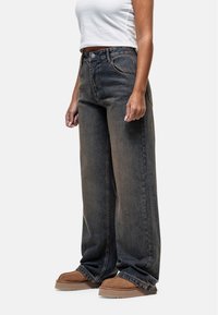 Jeans taille haute, coupe large en denim foncé avec une finition délavée, comportant des poches standard et une fermeture à bouton à la taille.