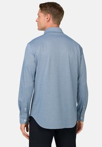 Camicia azzurro chiaro a maniche lunghe con bottoni, realizzata in tessuto morbido, presenta un colletto a punta e un orlo curvo con polsini con bottoni.