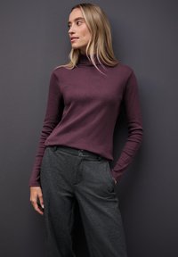 Maglione a maniche lunghe bordeaux con colletto alto abbinato a pantaloni larghi grigio scuro, caratterizzati da una texture liscia e una silhouette aderente.
