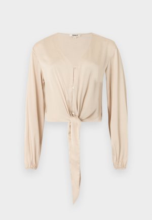 Bézs színű, hosszú ujjú blúz V-nyakkal, elülső gombokkal, gumírozott mandzsettákkal és deréknál megkötött szövetdísszel.