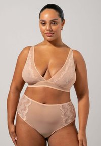 Bralette med spetskanter och högmidjade trosor i nude, med genomskinligt tyg och dekorativa spetsdetaljer på sidorna. Slät textur.