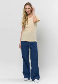 Világos sárga V-nyakú póló és kék, laza szabású nadrág. A póló rövid ujjú; a nadrág zsinórral állítható és kényelmes lábszára van.