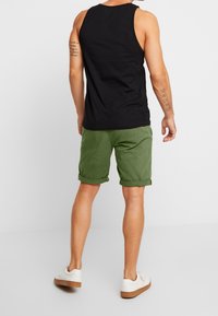 Débardeur noir, shorts verts remontés et baskets blanches. Mise sur un tissu décontracté et léger avec un design simple. Pas de motifs ni d'accents.