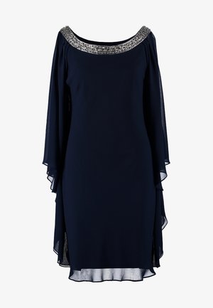 Granatowa sukienka z przezroczystymi rękawami w kształcie peleryny, ozdobnym dekoltem i swobodnym krojem, w połączeniu z czarną kopertówką i wysokimi obcasami.