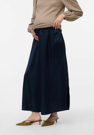 Marineblauwe satijnen maxi-rok met een elastische tailleband en zijsplitten, gecombineerd met groene puntige schoenen en een getextureerde beige top.