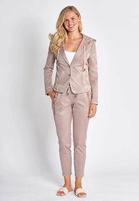 Light pink tracksuit with a structured, hooded jacket featuring palm leaf patterns and matching tapered pants, made of smooth, stretchy fabric.