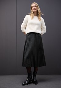 Maglione crema e morbido abbinato a una gonna midi nera a pieghe. Stivaletti neri con tacco leggero, superficie liscia e hardware minimale.