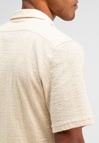 Korte mouwen overhemd van geweven lichtbeige stof, met een klassieke kraag en een ontspannen pasvorm met subtiele geweven patroon details.