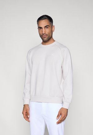 Jasnobeżowa bluza wykonana z miękkiego materiału, z raglanowymi rękawami, ściągaczami na mankietach i dolnym brzegu oraz subtelnym logo na piersi.