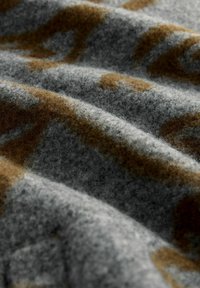 Grå uldstof med en blød texture, prydet med brune abstrakte mønstre, der er blandet ind i overfladen, hvilket skaber et dæmpet men alligevel tydeligt design.