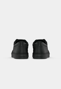 Black leather sneakers with a textured finish, flat sole, and padded collars. "Calvin Klein" branding on the heel. Rear view.