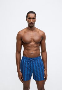 Calções de banho azuis para homem com cintura de cordão, apresentando riscas verticais, textura leve e suave, e corte atlético.