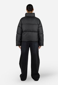Svart boblejakke med høy krage, blokk-quiltet design og store ermer. Kombinert med vide mørke jeans.