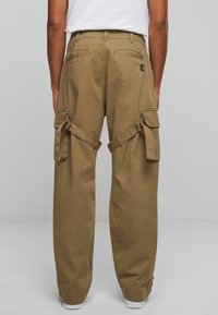 Khaki cargobyxor med en avslappnad passform, som har sidofickor, justerbara remmar och en logopatch på baksidan. Tillverkat av bomull.